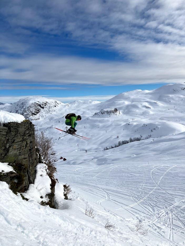 Ein person på ski hoppar ned frå ein kant i eit vinterlandskap. - Klikk for stort bilde